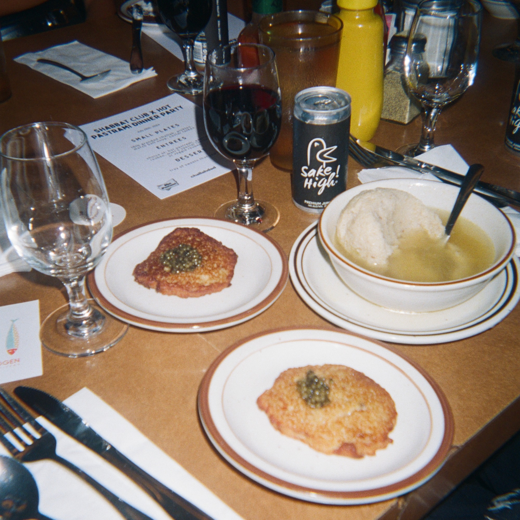 Place setting at a Shabbat Club dinner with latkes and caviar, matzo ball soup and wine