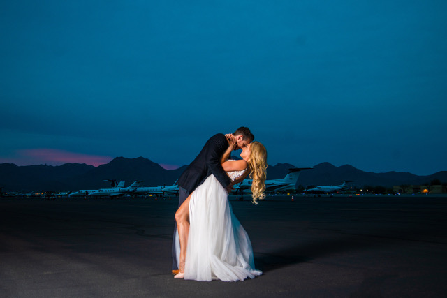A couple sharing a kiss on the runway at dusk, the McDowell Mountains and parked jets behind them