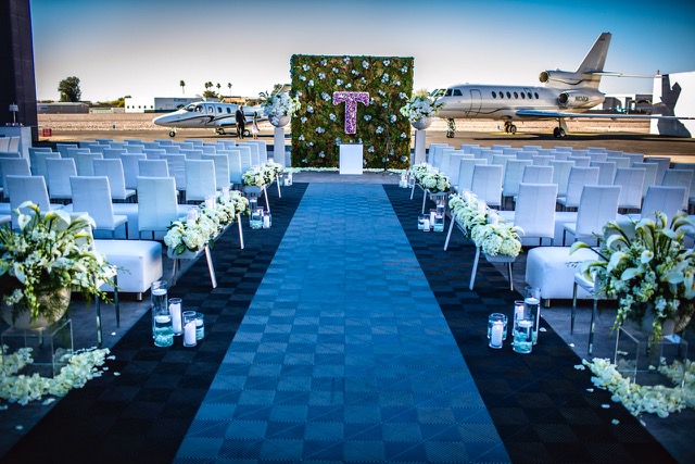 A wedding ceremony set on the Scottsdale Airport ramp, white chairs and florals lining the aisle with private jets behind