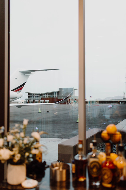 A private jet seen through the window beside a table of whiskey and florals