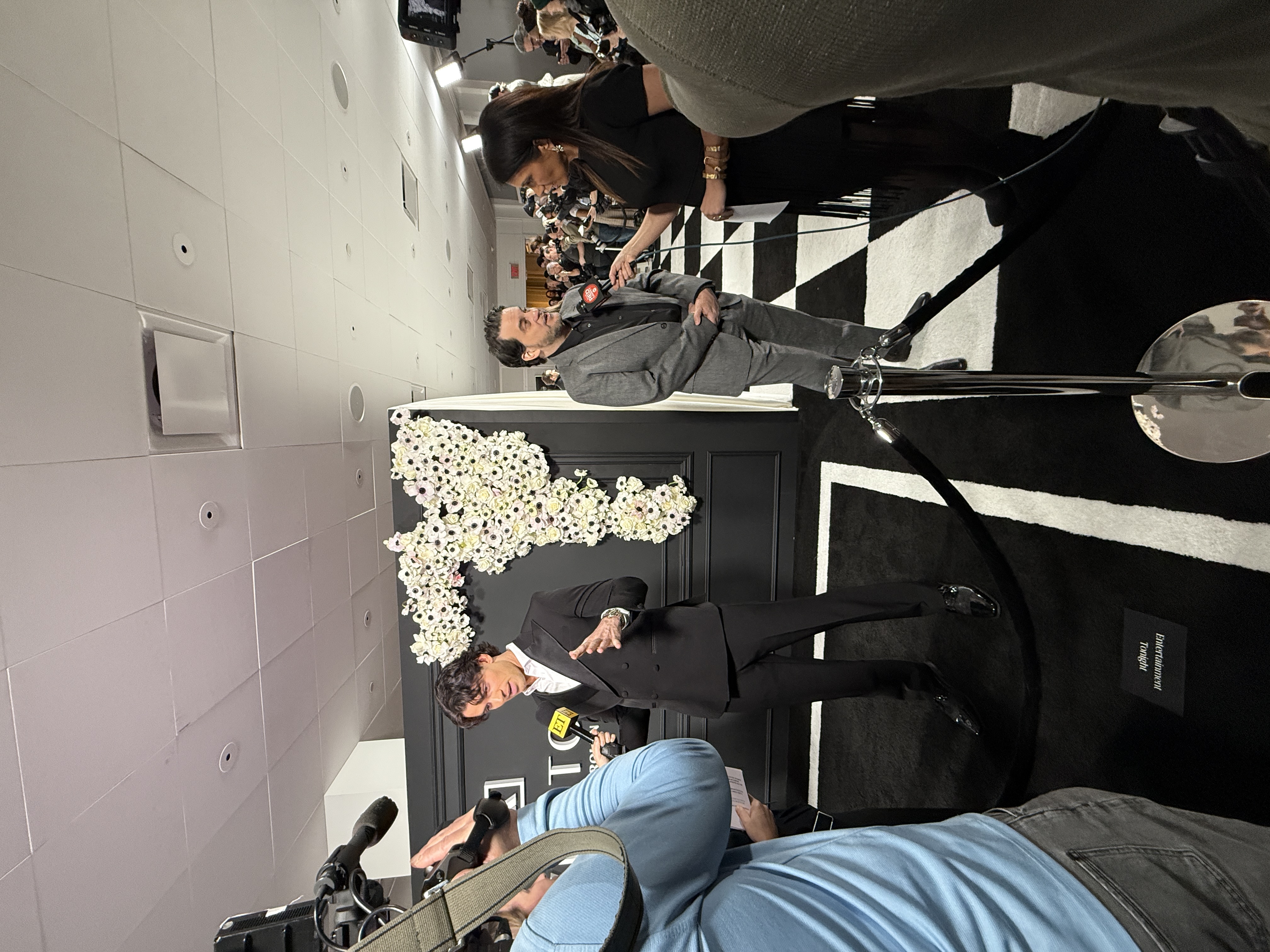 Red carpet press line with reporters interviewing guests in front of a floral backdrop
