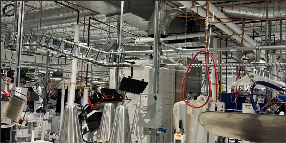 Overhead conduit, piping and electrical panels installed above equipment inside a commercial laundry facility.
