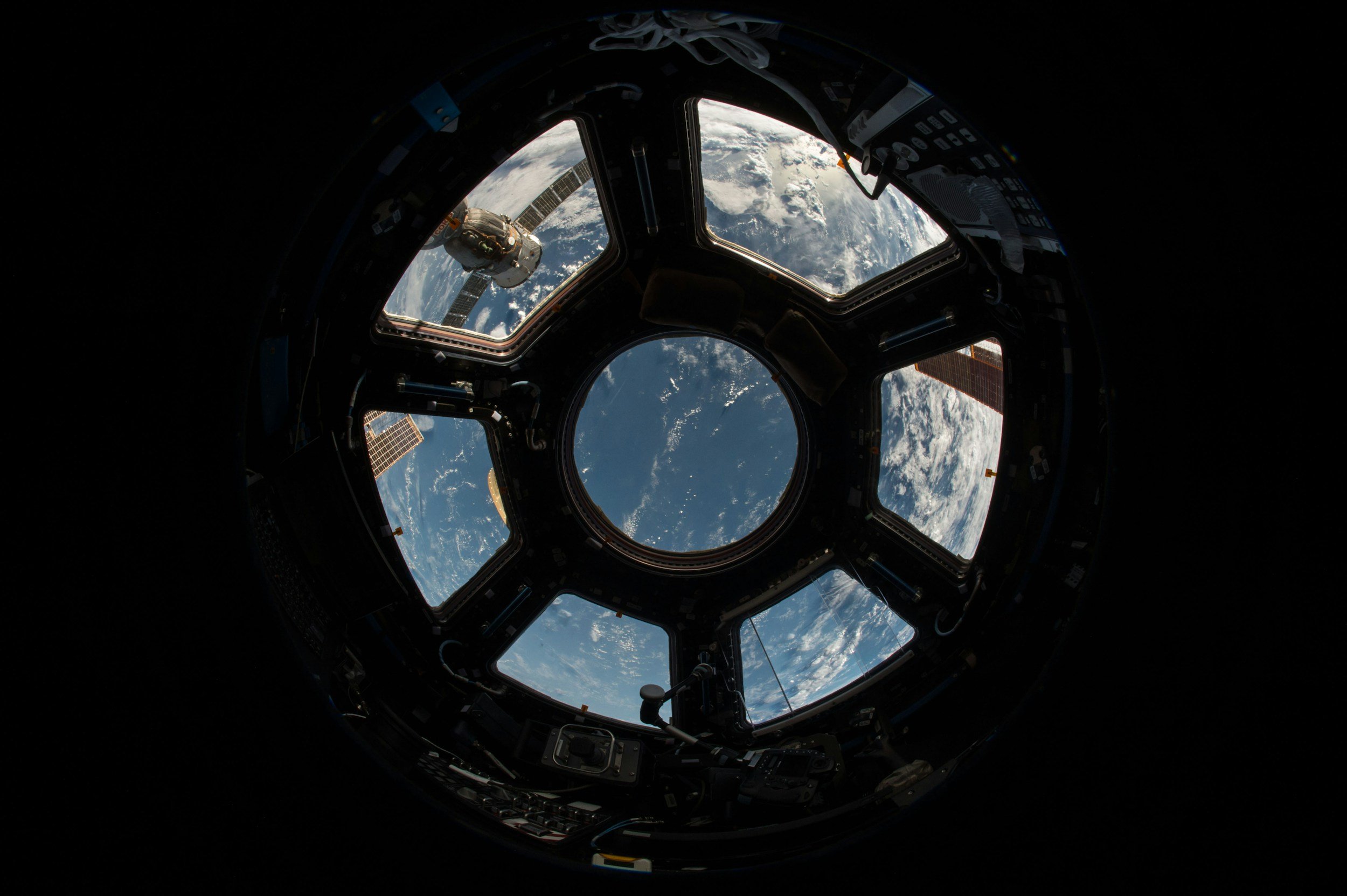 View of Earth from inside the International Space Station window with a spacecraft and solar panels visible outside.