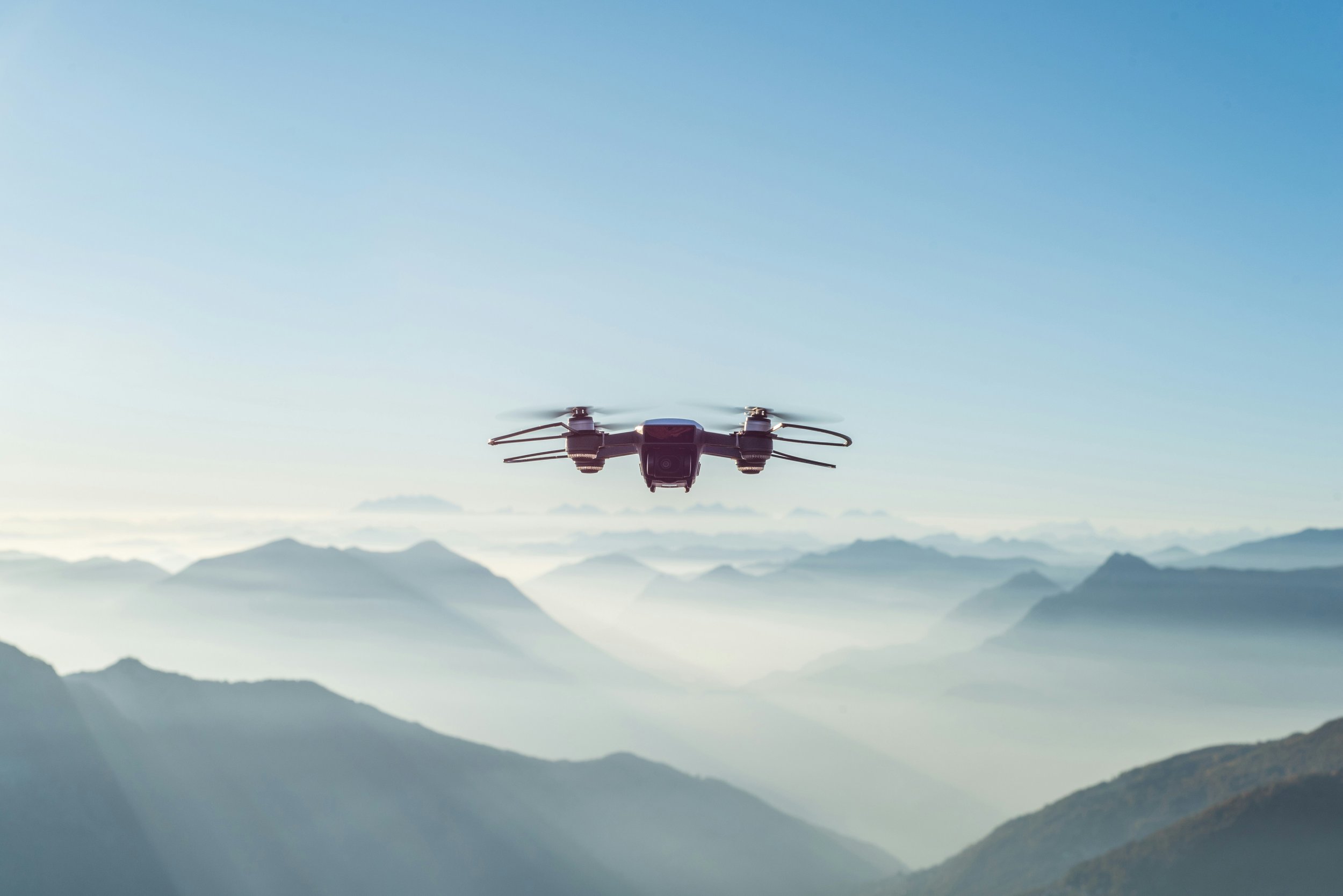 A drone flying over a mountain range with mist and blue sky in the background.